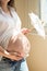 Pregnancy. A pregnant woman stands near a window and holds an openwork white umbrella.