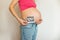 Pregnant belly girl with ultrasound in her hands on a light background. Smiling young pregnant in jeans woman hugs her