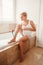 Pregnant blonde Caucasian woman shaving legs in bathroom