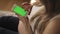 Pregnant blonde woman sitting on sofa using smartphone with green screen