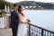 A pregnant bride in a wedding dress is standing on the dock, admiring the view of the river, behind her hugs her husband