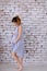 Pregnant cauca european sian woman wearing blue dress standing in brick wall background and holding belly.