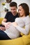 Pregnant Couple Sitting On Sofa With Man Touching Womans Stomach