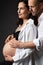 Pregnant Couple in White Shirts embracing Belly over Black Background. Mother and Father Love expecting Baby during Pregnancy.