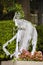 Pregnant ghost-zombie outside Halloween decoration in front of a house and a hedge with flowers at bottom