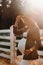 A pregnant girl with a big belly in a hat near a horse corral in nature at sunset.Stylish pregnant woman in a brown dress with