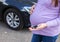 A pregnant girl with a big belly holds a car key in her hand. Known for the dangers of driving a car during pregnancy, the threat