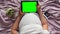 A pregnant girl flips through a digital tablet with a green screen. Top view of a pregnant girl lying in bed with a