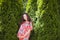 Pregnant girl near beautiful greenery. Beautiful pregnant woman in dress and touching belly stands near thuja. Future mother in a