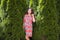 Pregnant girl near beautiful greenery. Beautiful pregnant woman in dress and touching belly stands near thuja. Future mother in a