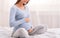 Pregnant Girl Smiling Sitting On Bed In Cozy Bedroom, Cropped