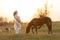 A pregnant girl in white communicates with a horse on a green meadow at sunset. Therapy and relaxation for pregnant women.