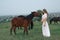 A pregnant girl in white communicates with a horse on a green meadow. Therapy and relaxation for pregnant women