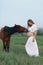 A pregnant girl in white communicates with a horse on a green meadow. Therapy and relaxation for pregnant women