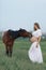 A pregnant girl in white communicates with a horse on a green meadow. Therapy and relaxation for pregnant women