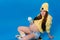 a pregnant girl in yellow clothes with a glass of juice sits on a skateboard on a blue background