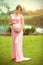 Pregnant happy woman caressing her belly in summer park. Full length pregnant beauty woman outdoor portrait. Healthy pregnancy