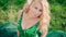 Pregnant lady with white orchids in blond hair, sitting on the grass in a long gorgeous green dress with emerald