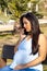 Pregnant Latina woman talking on cell phone sitting in park