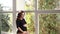 Pregnant moman sits in front of big window. Model dressed in black bodysuit. She put her hand on the belly. Happy future