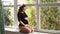 Pregnant moman sits in front of big window. Model dressed in black bodysuit. She put her hand on the belly. Happy future