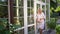 Pregnant in white dress standing near door in garden in backyard.