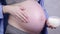 Pregnant woman applying stretch mark cream to belly- pregnancy, people and maternity concept