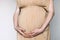 Pregnant woman in beige dress touching belly, preparing go to maternity hospital for childbirth. Pregnancy, maternity