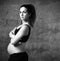 Pregnant woman with belly, in black sport pants and top, pink sneakers. Hands on hips. Posing on gray background. Full-length