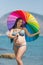 Pregnant woman in bikini with iridescent parasol against sea