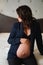a pregnant woman in a black jacket with bare breasts and a belly on the bed