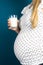 Pregnant woman on blue background holding a glass of milk, delivering calcium