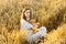 A pregnant woman in a blue dress holds a stuffed bear toy and sits in a field