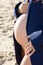 Pregnant woman closeup holding belly in man blue jacket standing on sand beach