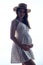 Pregnant woman in country style summer dress and straw hat standing touching her belly