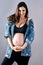 A pregnant woman in a denim jacket with hands on her belly
