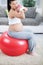 pregnant woman doing bicep muscle exercises using dumbbells while seated on a fitness ball