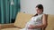 Pregnant woman doing breathing exercise experiencing contractions while sitting on the couch