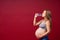 A pregnant woman drinks water on a red background. Thirsty. Enjoys the taste of pure water. Pregnancy Lifestyle. Copy space