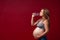 A pregnant woman drinks water on a red background. Thirsty. Enjoys the taste of pure water. Pregnancy Lifestyle. Copy space