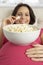 Pregnant Woman Eating Bowl Of Popcorn Sitting On Sofa At Home