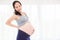 Pregnant woman having backache standing over bright window