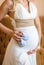 Pregnant woman holding bump in white dress, close-up