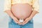 Pregnant woman is holding cream in front of her belly. Close up, isolated