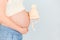 Pregnant woman is holding knitted beige children hat in front of her belly waiting for child& x27;s birth