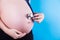 Pregnant woman holding phonendoscope on her belly on blue background