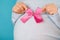 Pregnant woman holding pink bow on tummy belly background. Young girl expecting baby. Maternity, motherhood, pregnancy