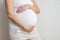 Pregnant woman holds hands on belly on light background. Pregnancy, maternity, preparation and expectation concept. Close-up, copy