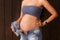 Pregnant woman in jeans shorts and blue top holds hands on belly on a dark brown background. Pregnancy, maternity. Beautiful tende