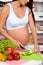 Pregnant woman in the kitchen cuts different vegetables on spring salad.